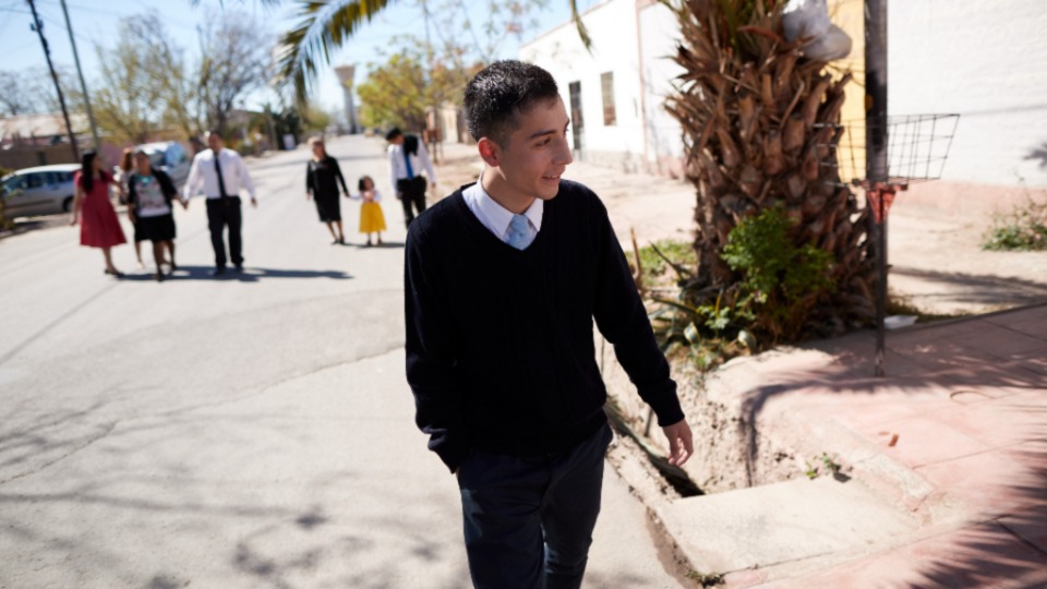 A young man walks down the street with his family on a Sunday afternoon. 